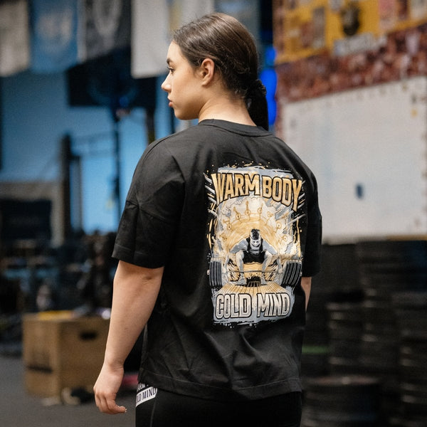 Person wearing a сotton black T-Shirt Lift Off with a graphic design and text on the back, standing in an indoor setting – Warm Body Cold Mind